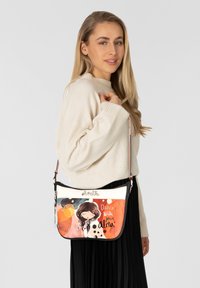 Bunte Umhängetasche mit einem bedruckten Design eines Mädchens, auf orangefarbenem Hintergrund mit schwarzen Punkten, aus synthetischem Material.