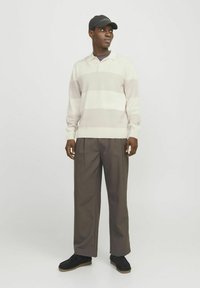 Lys beige og creme stribet pullover med krave, parret med løse brune bukser og sorte sko, afsluttet med en sort kasket.