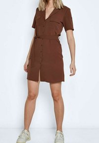 Hnědé krátké šaty s krátkým rukávem a výstřihem do V, propínací přední částí, dvěma náprsními kapsami a páskem v pase. Výrazný rozparek na boku.