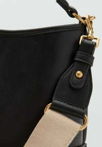 Angolo di una borsa a tracolla nera in pelle, caratterizzata da hardware dorato, una tracolla beige regolabile e una texture liscia con cuciture visibili.