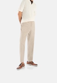 Beige broek, licht gebreide polo met een brede kraag, en bruine leren schoenen met witte zolen. Gladde textuur en elegante pasvorm.