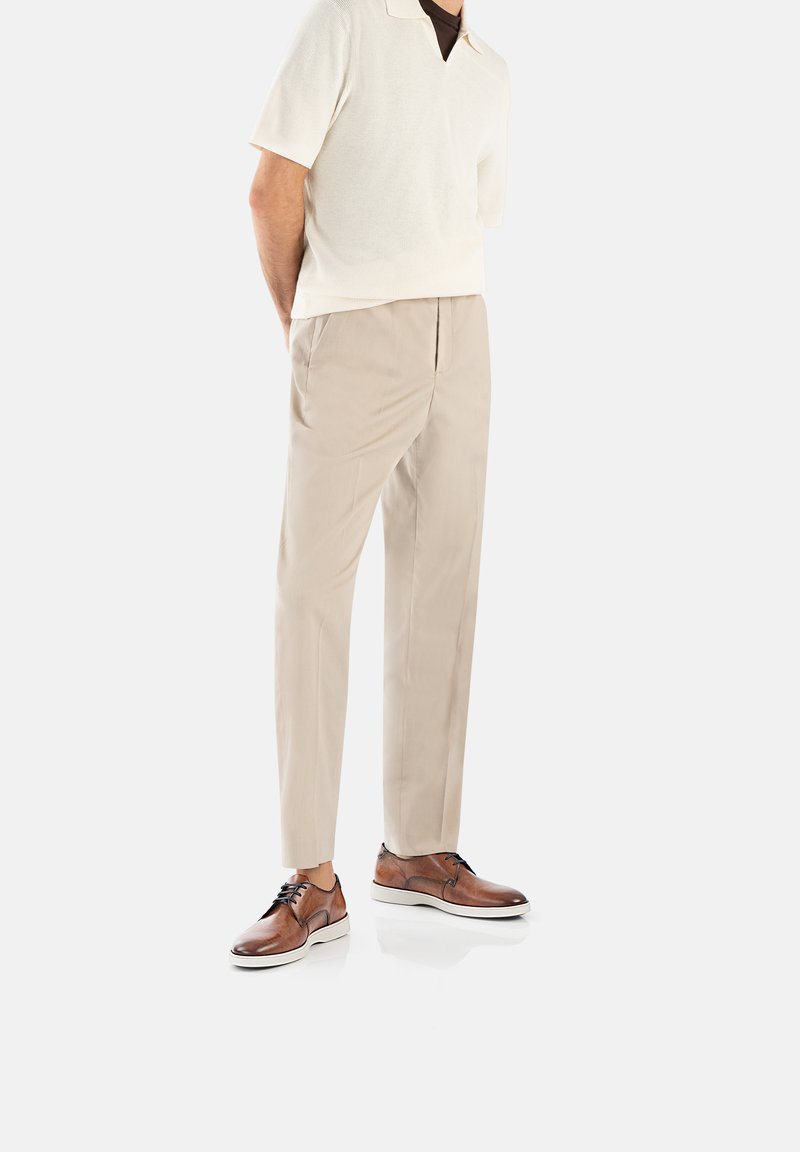Beige broek, licht gebreide polo met een brede kraag, en bruine leren schoenen met witte zolen. Gladde textuur en elegante pasvorm.