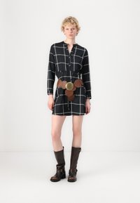 Rochie neagră cu model în carouri albe, mâneci lungi, închidere cu nasturi. Curea din piele maro cu accente circulare. Botine maro până la genunchi.