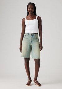 Svetlo modri denim Bermuda kratki hlače z visokim pasom, petimi žepi in rahlo izblisoranim videzom, v kombinaciji z belo majico na naramnice in sandalmi.