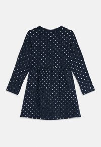 Mørkeblå langermet kjole med beige prikker, samlet liv, og rund halslinning, liggende flatt på en hvit bakgrunn.