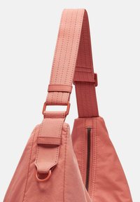 Różowy materiałowy pasek na ramię z regulowanym hardwarem i szczegółowymi ściegami. Posiada zamek błyskawiczny w pasującej torbie, podkreślając elegancki design.