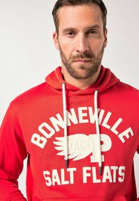 Felpa con cappuccio in cotone rosso con stampa grafica con la scritta "BONNEVILLE RACE SALT FLATS" in bianco. Include coulisse con punte nere.