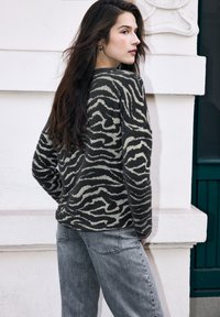 Sweter w paski w kolorze czarnym i beżowym z miękkiego, puszystego materiału, zestawiony z jasnoszarymi jeansami. Ubranie ma luźny krój i luźne rękawy.