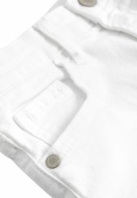 Weißer Denim-Stoff mit einer Vordertasche und silbernem Metallknopf-Detail. Glatte Textur mit sichtbaren Nähten und einem leichten Glanz.