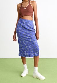 Jupe fleurie bleue de longueur midi, associée à un crop top marron. Des baskets blanches et des chaussettes courtes côtelées complètent le look.