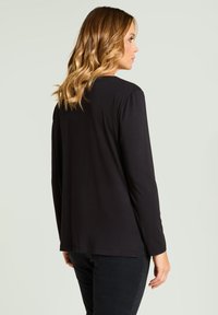 Schwarzes Langarmshirt aus weichem Stoff mit entspanntem Schnitt und abgerundetem Saum. Das Design ist minimalistisch, ohne sichtbare Muster oder Akzente.