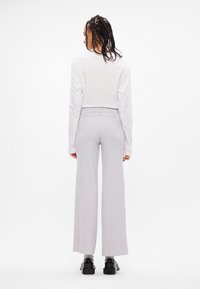 Top branco de manga longa, calças largas cinza claro com textura canelada, combinadas com sapatos de plataforma pretos. Vista de costas.