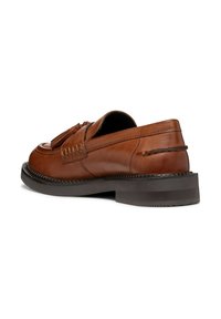 Scarpa in pelle marrone a slip-on con punta arrotondata, nappine decorative e suola scura texture. Presenta cuciture visibili e dettagli laterali.