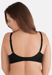 Zwarte bh met verstelbare bandjes, zachte textuur en haak-en-oogsluiting op de rug. Heeft gegolfde rand langs de band.