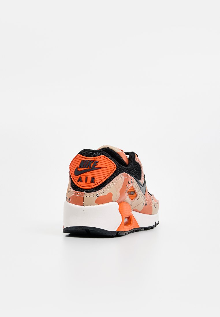 Zapatillas Nike Air con un diseño de camuflaje en tonos melocotón y naranja, con una parte superior de malla negra y suela de goma texturizada.