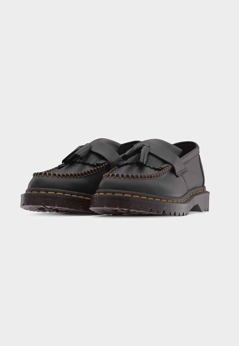 Black leather tassel loafers with fringed vamps, yellow stitching, and thick grooved rubber soles on a white background.