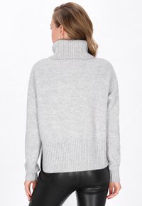 Maglione grigio con colletto a cilindro e orlo a costine. Tessuto morbido, vestibilità rilassata, fessure laterali e maniche lunghe. Indossato con leggins neri.