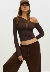 Hnědý off-shoulder dlouhý rukáv top vyrobený z elastického materiálu, spárovaný s tmavě hnědými elastickými kalhotami v pase se bočními kapsami.