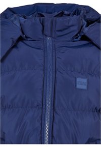 Giubbotto imbottito blu navy con colletto alto, chiusura centrale con zip e un patch logo quadrato, realizzato in tessuto morbido e isolante.