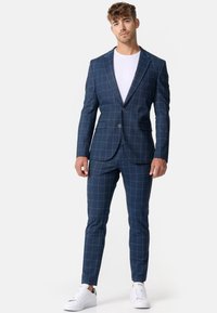 Marineblå ternet jakkesæt med en blazer med notched lapels, to knapper og matchende bukser, parret med en hvid t-shirt og hvide sneakers.