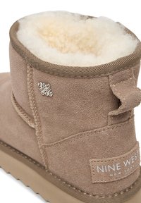 Beige suede winter boot with fluffy white fleece lining and Nine West New York label on the heel.