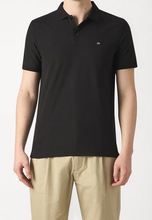 Schwarzes Polohemd aus Baumwolle, mit klassischem Kragen, drei Knöpfen und einem dezenten "ck"-Logo auf der Brust. Glatte Textur.