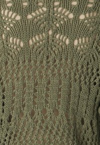 Tissu en maille vert olive présentant un motif ajouré avec des motifs de feuilles, offrant un design texturé et respirant.