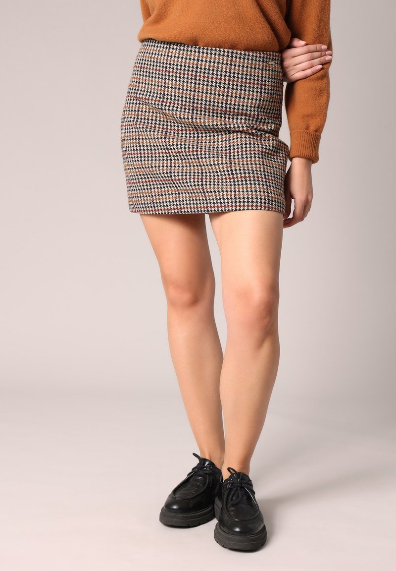 Bruine geruite minirok met een fitted vorm. Gemaakt van textuurstof, met een mix van beige, bruin en rode tinten. Zwarte veterschoenen.