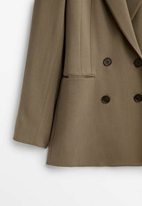 Blazer doppio petto marrone con rever a gradino, due tasche frontali e tessuto texture. I bottoni sono neri e rotondi.