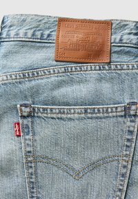Lichtblauwe denim jeans met een bruine leren patch op de achterkant, een rode Levi's-label op de zak en zichtbare stiksels.