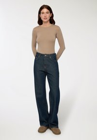 Maglietta beige a maniche lunghe abbinata a jeans a vita alta blu scuro con cinque tasche e hardware color rame. Calzature color cammello completano l'outfit.