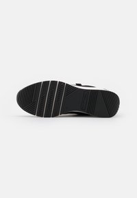 Black athletic shoe sole with textured grip pattern, angular lines, and a small logo; designed for durability and traction on various surfaces.