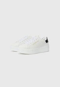 Baskets en cuir blanc avec une finition texturée, semelle plate blanche, bout rond et accents de talon noirs. Logo de la marque en or sur le côté.