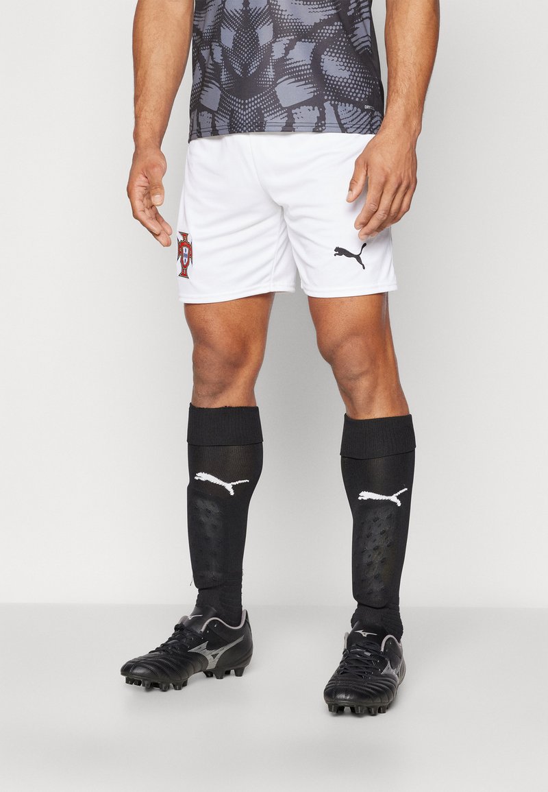 Pantaloni corti bianchi con lo stemma del Portogallo, camicia grigia a motivo, calze nere con logo Puma e scarpe da calcio nere con dettagli argento.