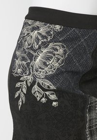 Jupe noire et bleu foncé avec des motifs patchwork et des dessins floraux blancs brodés près de la ceinture.