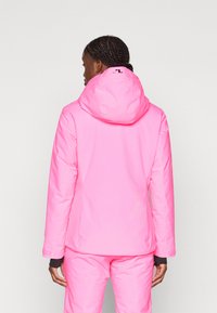 Chaqueta rosa brillante con capucha, textura suave, con un logo en el cuello, diseñada para un look ajustado y exterior. Acompañada de pantalones a juego.