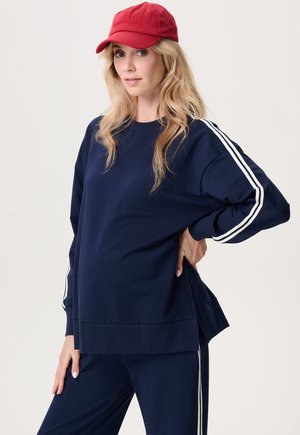 Marineblauwe sweatshirt met witte zijstrepen, gemaakt van zachte stof. Heeft een losse pasvorm en zijsplitten voor comfort. Gecombineerd met bijpassende broek.