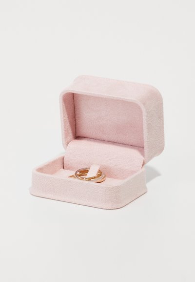 Cutie de bijuterii din suede roz, cu o textură moale, având un interior compartimentat și afișând două inele de aur în interior. Design închis, cu margini rotunjite.