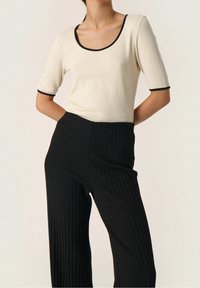 Cream knit top with black trim, paired with ribbed black wide-leg pants. Features fitted sleeves and a scoop neckline.