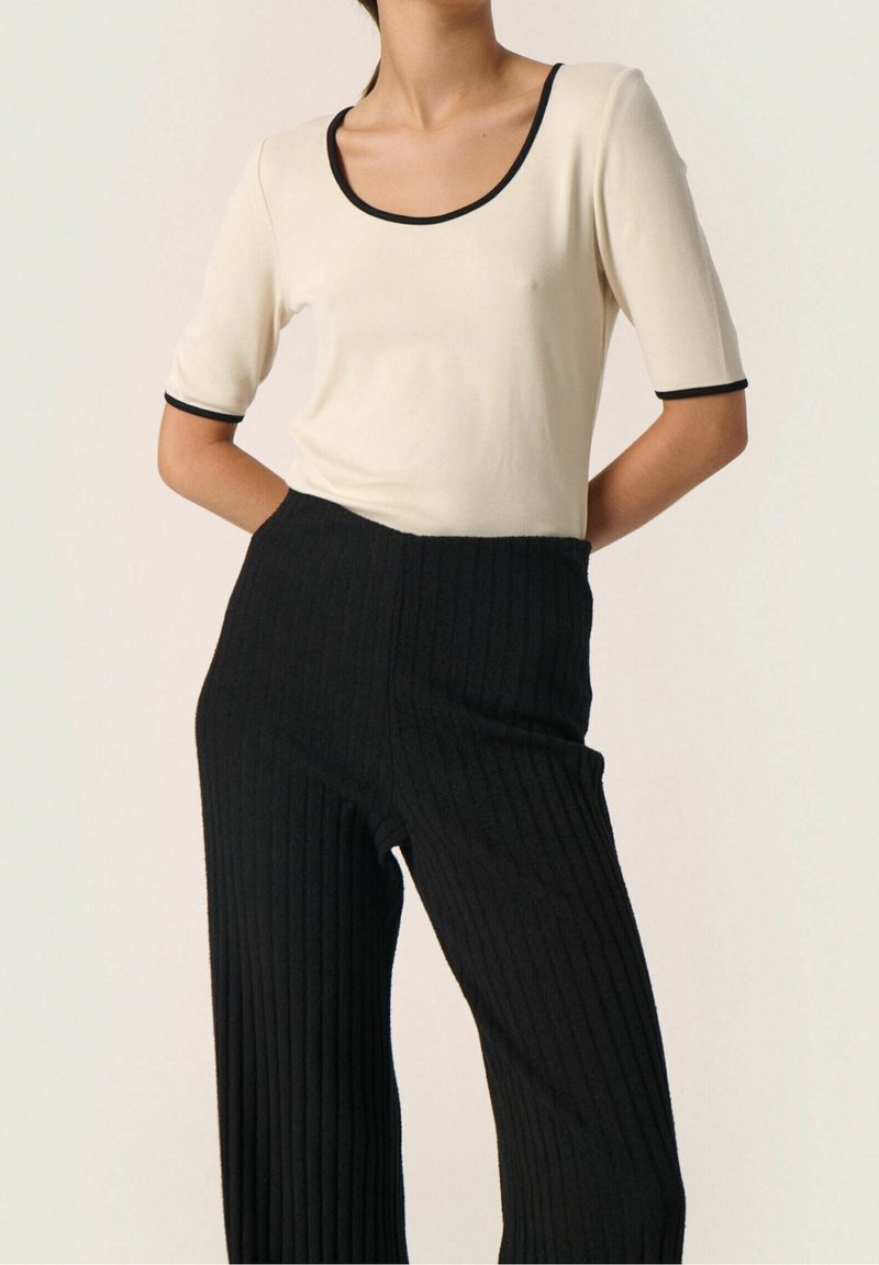 Cream knit top with black trim, paired with ribbed black wide-leg pants. Features fitted sleeves and a scoop neckline.
