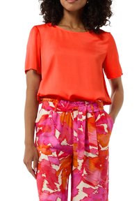Czerwony satynowy top z krótkim rękawem w połączeniu z różowymi spodniami w kwiatowy wzór z pomarańczowymi akcentami i paskiem w talii, zaprojektowanymi z myślą o komforcie.