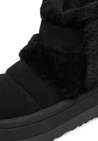 Stivale invernale nero con foderatura di pelliccia spessa attorno alla caviglia e suola liscia opaca, progettato per calore e comfort nelle giornate fredde.