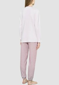Maglietta a maniche lunghe di un leggero color rosa con scollatura rotonda, abbinata a pantaloni da pigiama a righe rosse e bianche, con polsini elastici e vestibilità morbida.