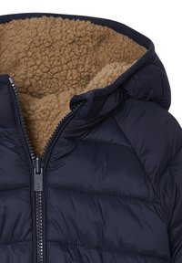 Dunkelblaue Steppjacke mit Reißverschluss, ausgestattet mit einem flauschigen, tanfarbenen Fleecefutter und gestepptem Design. Sie verfügt über eine Kapuze und detaillierte Nähte.