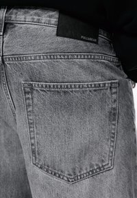 Harmaa farkut sisältävät takataskun ja mustan nahkalabelin, jossa on kohokuvioitu "PULL&BEAR" vyötäröllä. Raskaasti kulutettu, haalistunut pinta.