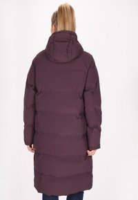 Giacca a vento viola con cappuccio, caratterizzata da pannelli cuciti orizzontali e un design di lunghezza media. Texture liscia e vestibilità rilassata.