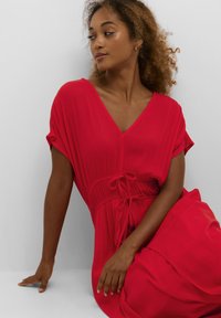 Robe rouge avec un décolleté en V profond, manches courtes et détail de taille cintrée. Fabriquée en tissu texturé avec une silhouette fluide.