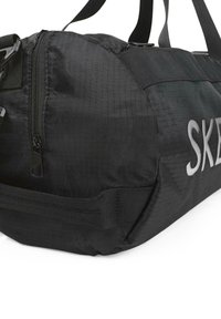 Bolsa de deporte negra hecha de un tejido duradero, con un bolsillo con cremallera, costuras reforzadas y el logotipo "SK" en blanco. Superficie texturizada y correas ajustables.