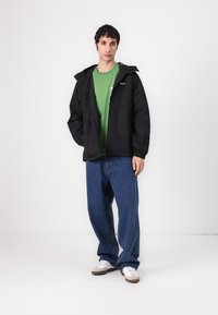 Black hooded jacket, green t-shirt, blue baggy jeans, and white sneakers. The jacket features a zip closure and elastic cuffs.