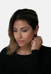Orecchini a cerchio rosa su una donna con capelli castani ondulati, che indossa una maglietta nera a maniche lunghe, con pelle leggermente texturizzata e trucco neutro.